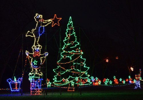Colorful Christmas lights display featuring a tree, stars, and a character holding a star, set against a dark night sky.