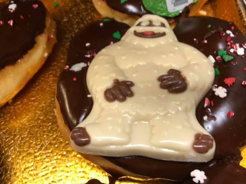 A chocolate-covered donut topped with a white chocolate yeti figure and festive sprinkles.