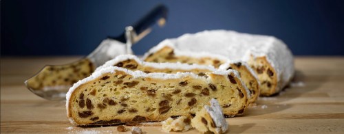 Sliced stollen bread dusted with powdered sugar, showcasing dried fruits and nuts on a wooden surface.