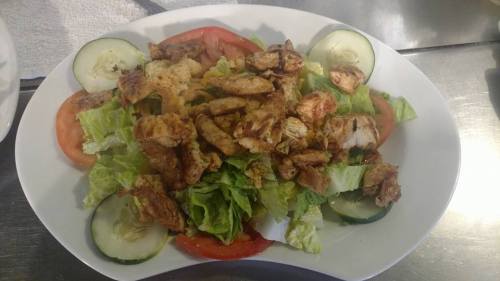 A fresh salad topped with grilled chicken, lettuce, tomatoes, and cucumber slices on a white platter.