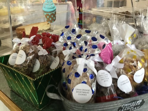 A display of assorted cookies in clear bags, tied with ribbons, labeled with flavors like peanut and chocolate chip.