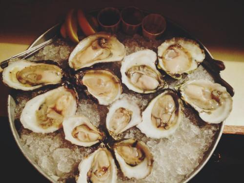 A platter of fresh oysters on ice, garnished with lemon slices and served with dipping sauces.