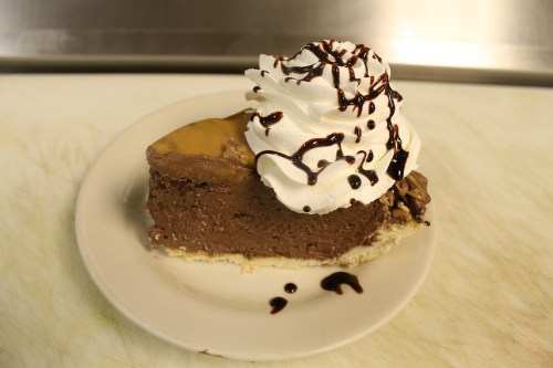A slice of chocolate pie topped with whipped cream and chocolate drizzle on a white plate.