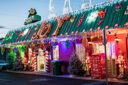A festive building adorned with colorful lights, decorations, and a large "JOY" sign, creating a cheerful holiday atmosphere.
