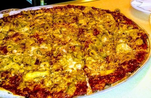 A close-up of a large pizza topped with green olives, cheese, and a golden-brown crust.