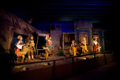 A colorful nativity scene with figurines depicting a village setting, featuring people and animals in a rustic environment.