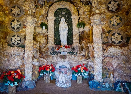 A decorated shrine featuring a statue of the Virgin Mary, surrounded by flowers and intricate stonework.