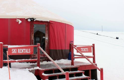 A red yurt with signs for ski rentals and tickets, surrounded by snow and a slope in the background.