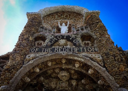 A stone grotto with a statue of Jesus, featuring the words "Grotto of the Redemption" against a blue sky.