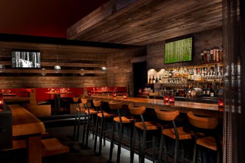Cozy bar interior with wooden decor, a well-stocked bar, and dim lighting, featuring red seating and wall art.