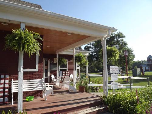 A sunny porch with white chairs and hanging ferns, leading to a green lawn and a red barn in the background.
