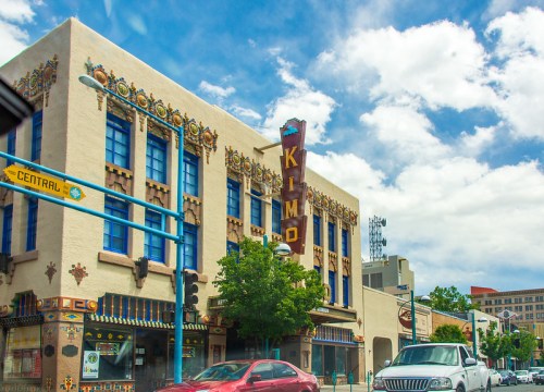 Historic Kimo Theatre building with colorful architecture under a blue sky, featuring decorative details and nearby traffic.