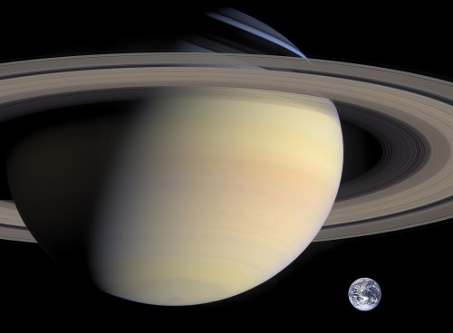A view of Saturn with its iconic rings, alongside a small Earth in the background, set against a dark space backdrop.