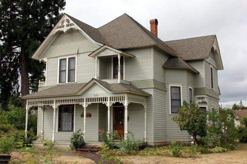 A charming two-story Victorian house with a gabled roof, decorative trim, and a front porch surrounded by greenery.