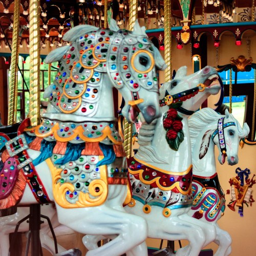 Colorful carousel horses adorned with jewels and intricate designs, set against a vibrant, decorative background.