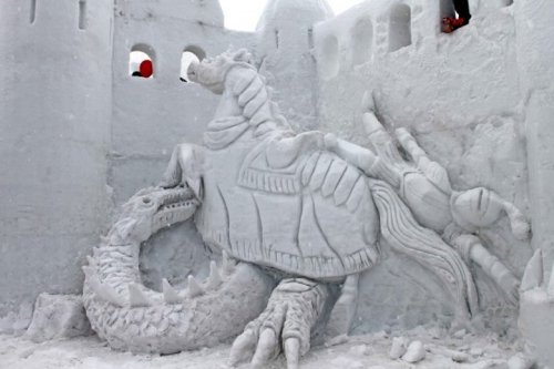 A detailed snow sculpture depicting a knight on a horse battling a dragon, set against a castle backdrop.