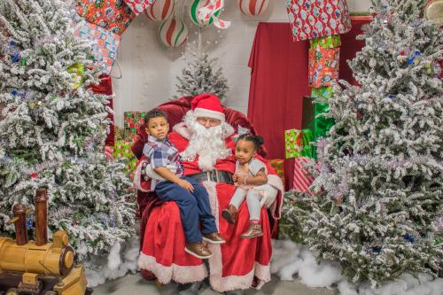 Two children sit on Santa's lap surrounded by festive decorations and Christmas trees.