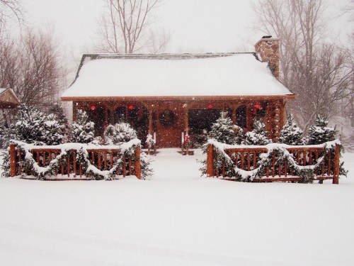 A cozy cabin covered in snow, surrounded by evergreen trees and festive decorations, creating a winter wonderland scene.
