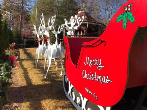 A festive red sleigh with "Merry Christmas" and white reindeer in a decorated outdoor setting.
