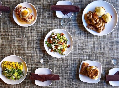 A top-down view of a table set with various dishes, including salads, eggs, and cinnamon rolls on white plates.
