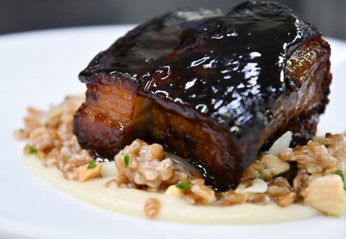A succulent piece of glazed pork belly served on a bed of grains with a creamy sauce, garnished with herbs.