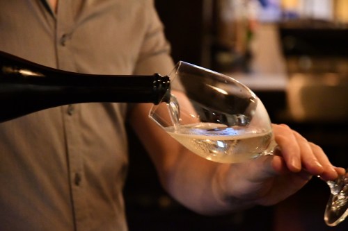 A person pours sparkling wine from a bottle into a glass in a dimly lit setting.