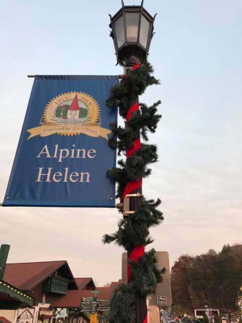 A festive street lamp adorned with greenery and a red ribbon, featuring a sign that reads "Alpine Helen."