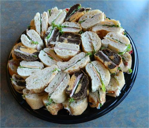 A large platter of assorted sandwiches, neatly arranged in a circular pattern, featuring various breads and fillings.