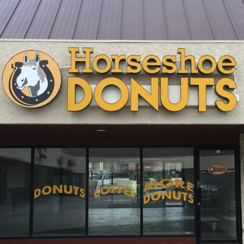 Sign for "Horseshoe Donuts" featuring a horse logo, with text promoting donuts and coffee.