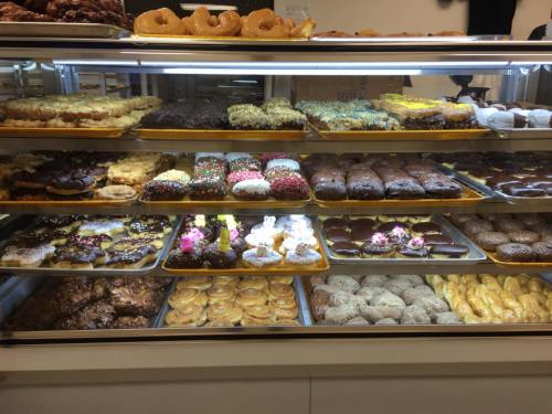 A display case filled with a variety of colorful donuts and pastries, including glazed, frosted, and sprinkled options.