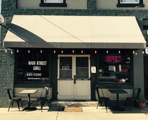 Exterior of Main Street Grill with an awning, open sign, and outdoor seating. Bright and inviting atmosphere.