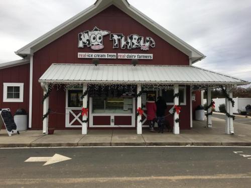 A red barn-style ice cream shop with a sign reading "Moo Thru," decorated for the holidays with wreaths and lights.