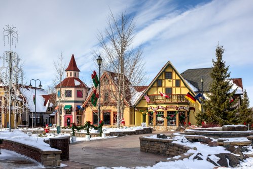 Charming winter village scene with snow-covered buildings, festive decorations, and a clear blue sky.