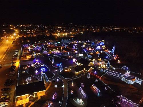 Aerial view of a festive park illuminated with colorful holiday lights at night, surrounded by a cityscape.