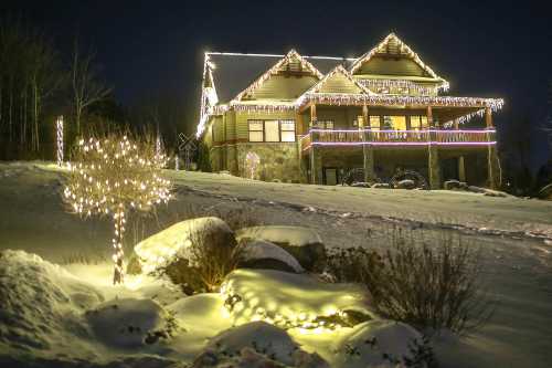 A beautifully lit house with holiday lights, surrounded by snow and decorated trees, glowing in the night.