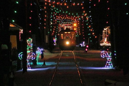 A festive scene with colorful holiday lights illuminating a snowy path and a train, surrounded by candy cane decorations.