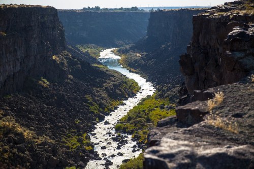 A winding river flows through a rocky canyon, surrounded by lush greenery and steep cliffs under a clear sky.