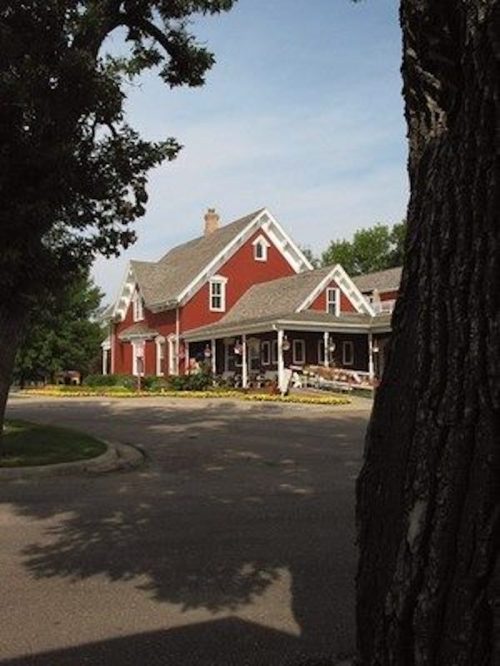 A charming red farmhouse with a gray roof, surrounded by trees and a clear blue sky.
