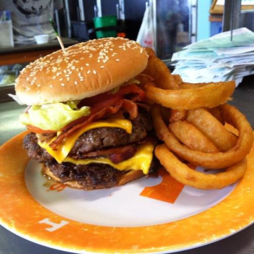 A towering cheeseburger with lettuce, bacon, and two patties, served with a side of crispy onion rings on a plate.