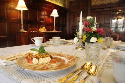 A beautifully set dining table with a plate of dessert, flowers, and elegant glassware in a cozy, vintage room.