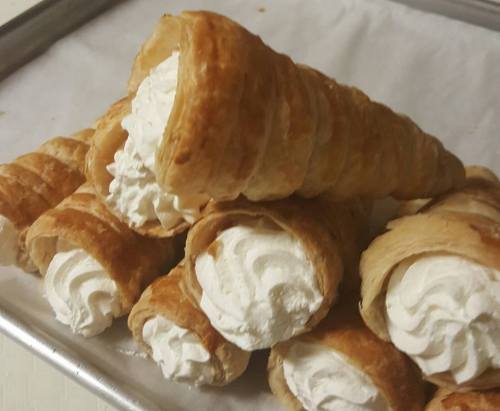 A tray of flaky pastry cones filled with whipped cream, stacked in a casual arrangement.