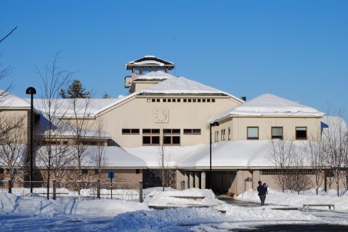 A snow-covered building with a clock tower and clear blue sky, surrounded by trees and a snowy landscape.