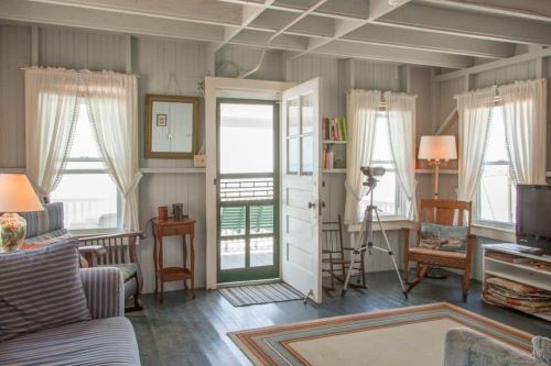 Cozy interior of a beach house with light-colored walls, a door leading outside, and comfortable furniture.