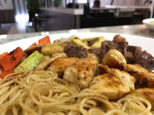 A plate of stir-fried chicken, beef, and colorful vegetables served with noodles.