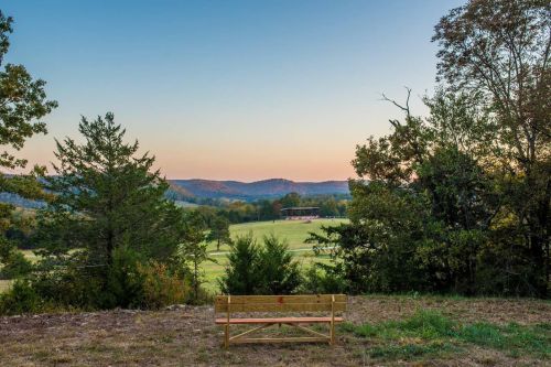 A wooden bench overlooks a serene landscape of rolling hills and trees at sunset.