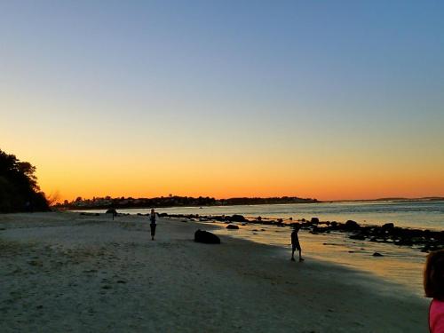 A serene beach at sunset, with silhouettes of people walking along the shore and gentle waves lapping at the sand.