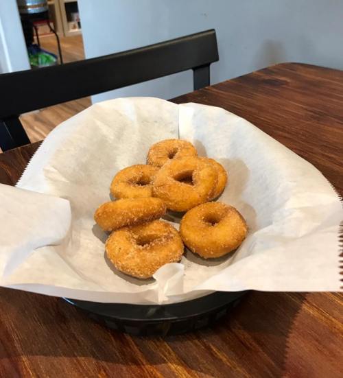 A basket of six golden, sugar-coated donuts on a wooden table.