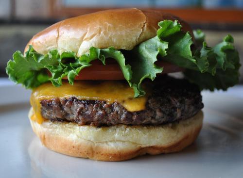 A juicy cheeseburger with melted cheddar, fresh lettuce, and a slice of tomato on a soft bun.