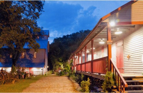 A scenic view of a rustic building at dusk, featuring a porch and surrounding greenery.