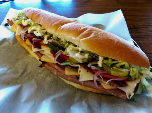 A large sub sandwich filled with various meats, cheese, lettuce, tomatoes, and condiments on a toasted hoagie roll.
